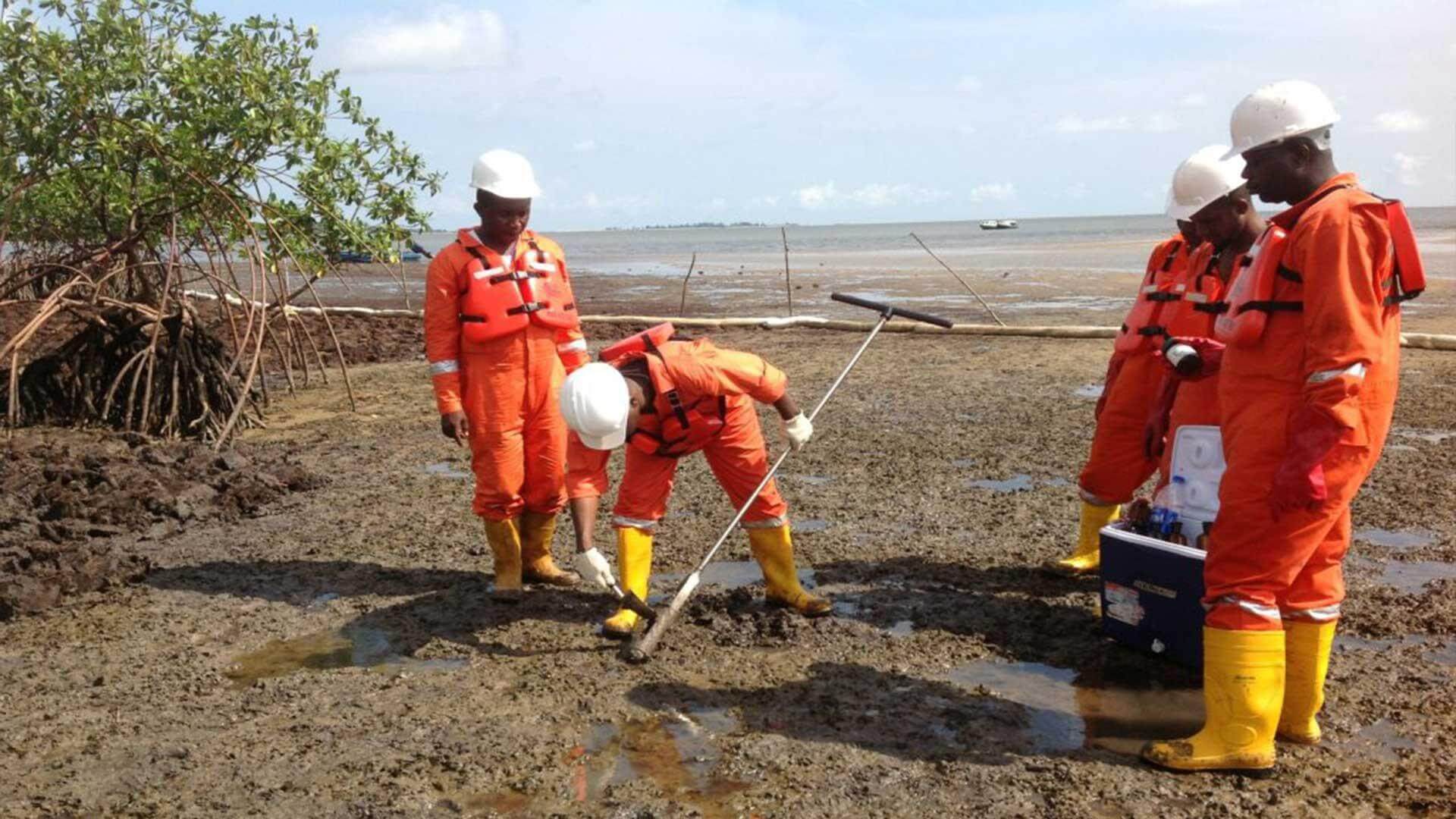 Technicians in protective equipment carrying out environmental sampling on a mudflat