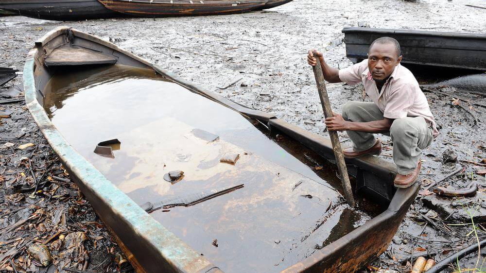 A fisherman in a wooden boat on a polluted shoreline