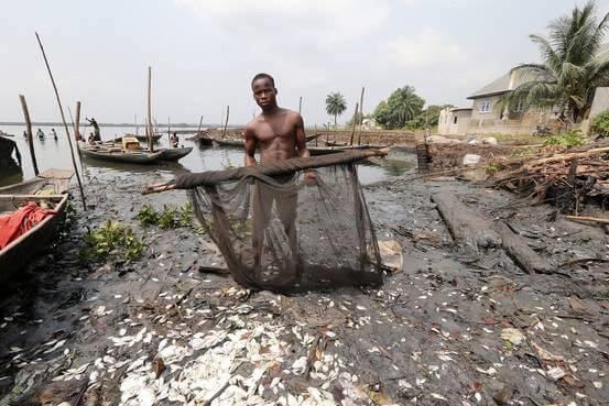 A fisherman stands in polluted water with an oil-stained net