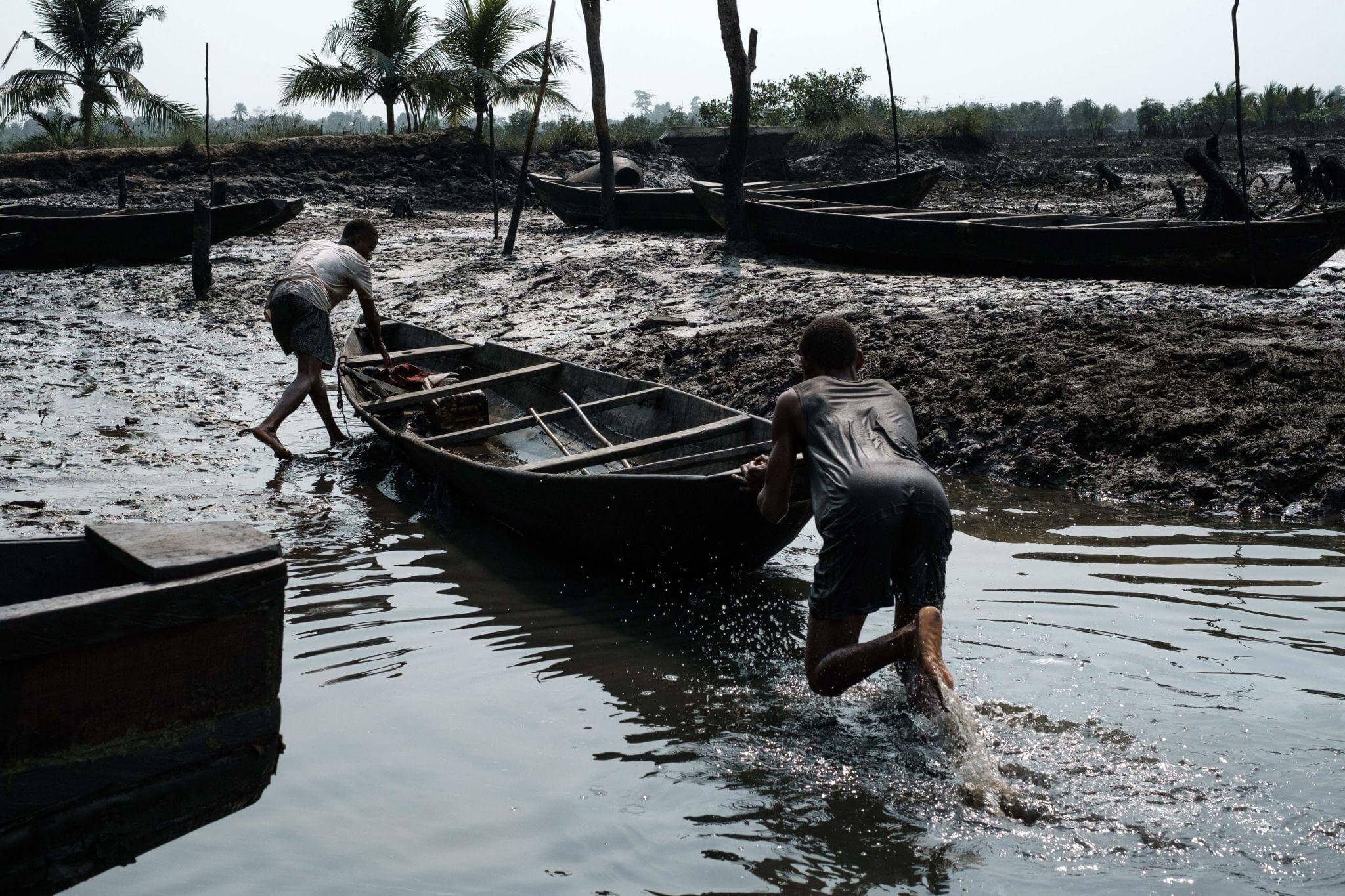 Community member moving wooden fishing boats through an affected creek
