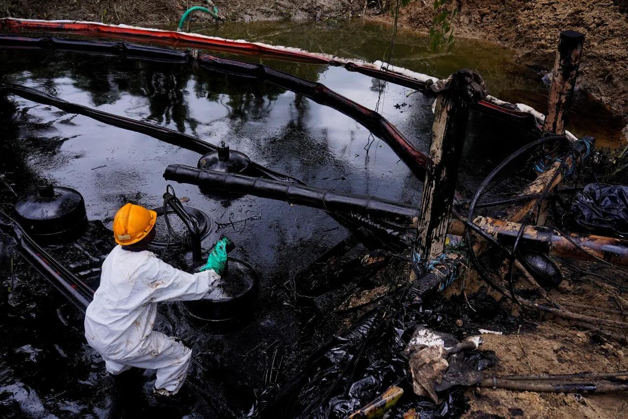 Responder in protective clothing working in oil-covered water behind a containment boom